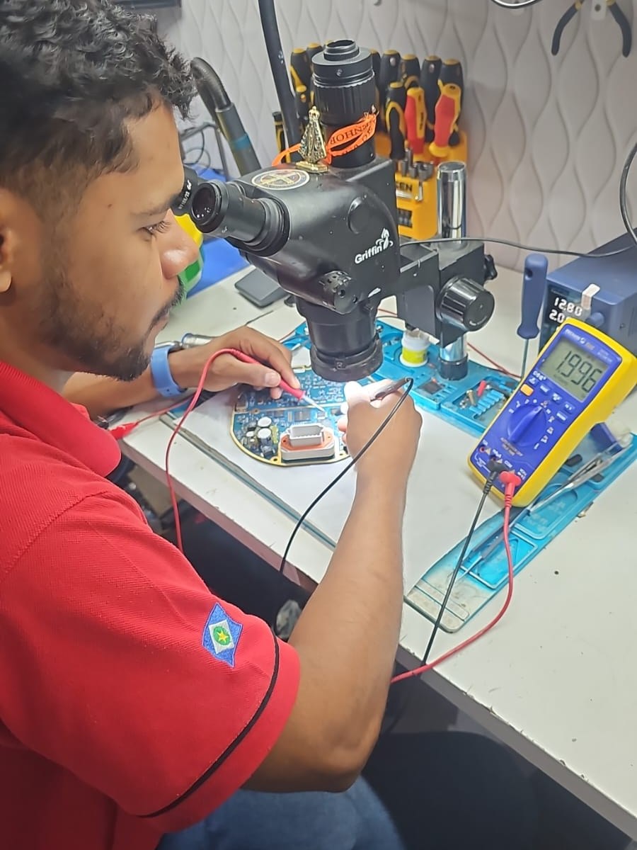 Técnico da Agro BS medindo componentes da placa de um monitor GPS com multímetro sob microscópio